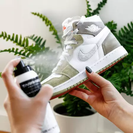 A view of a girl holding a white sneaker and spraying it