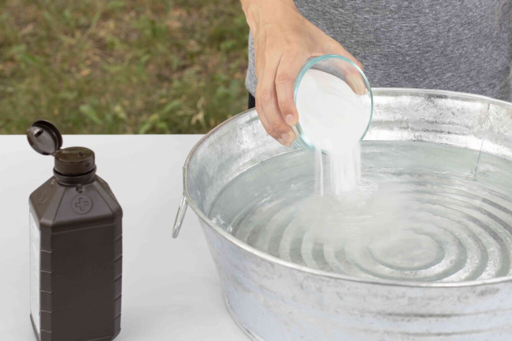 A view of a hand putting baking soda into bucket of water with hydrogen peroxide bottle on the side