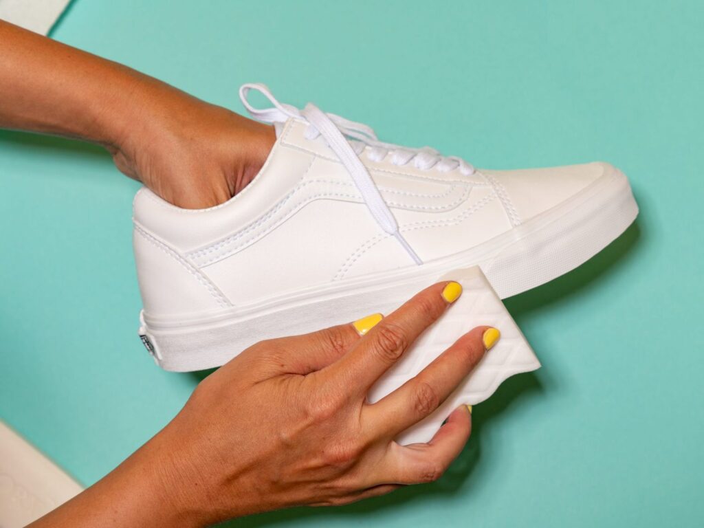 A view of a lady's hand cleaning a white sneaker with a white sponge