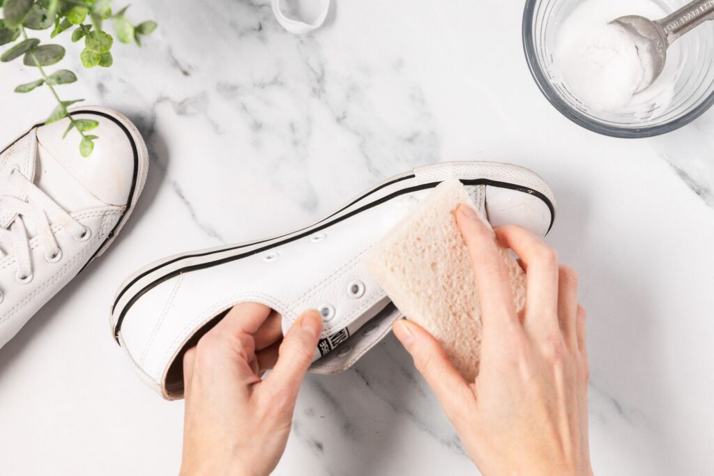 A view of a person cleaning white sneakers with a sponge with cornstarch mixture on the side