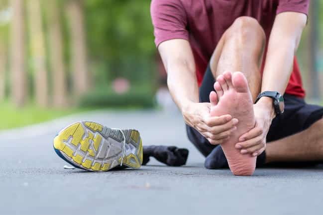 A view of a person holding thier foot sitting on road with one trainers off thier feet