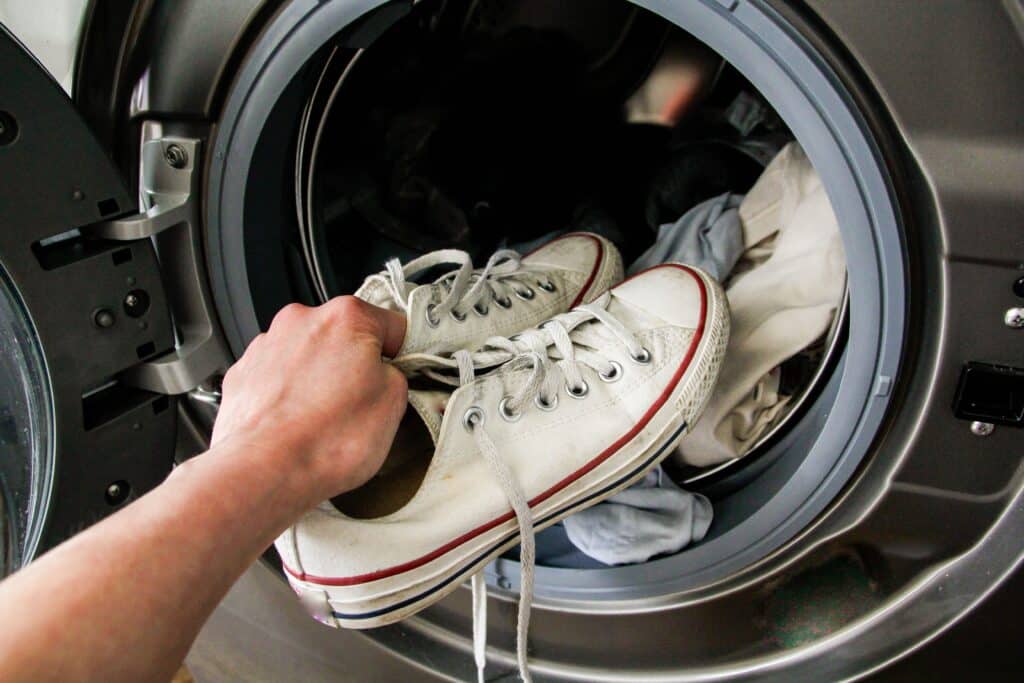 A view of a person putting white sneakers inside a washing machine