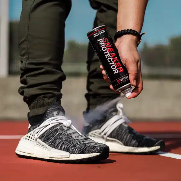 A view of a person spraying a sneaker protector spray onto thier gray and white shoes