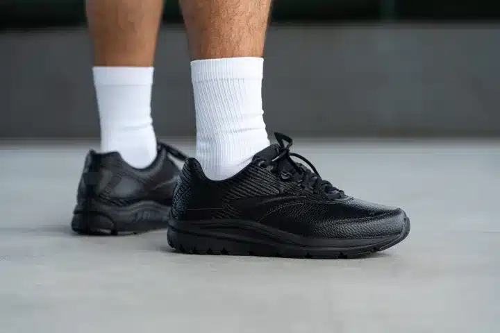 A view of a person wearing a black Brooks Addiction Walker sneaker with white socks