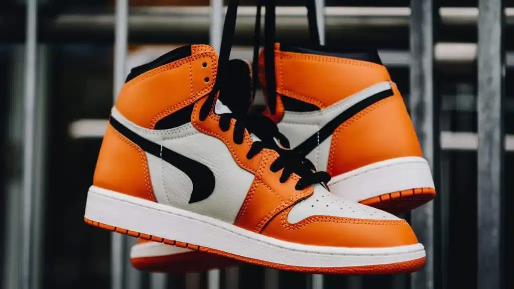 A view of orange and white air jordans hanging in the air by laces